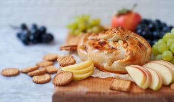 Baked Brie In Puff Pastry on a cutting board with apples and grapes
