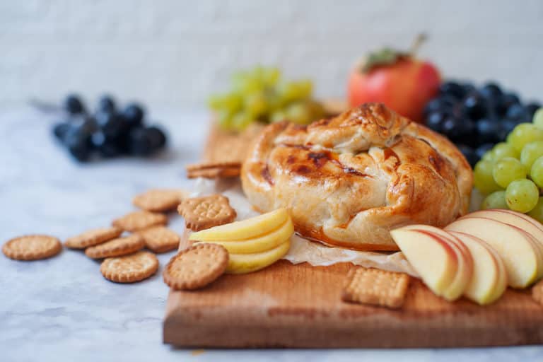 Baked Brie In Puff Pastry on a cutting board with apples and grapes