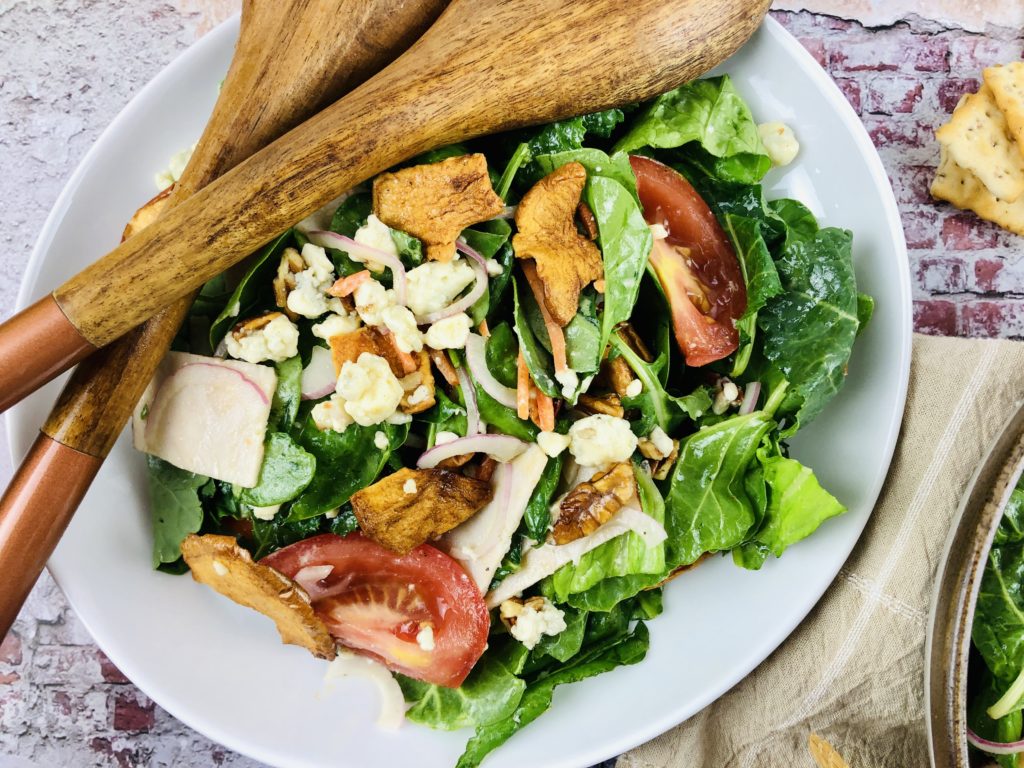 White Plate filled with Fuji Apple Salad and Dressing with wooden spoons on the side 