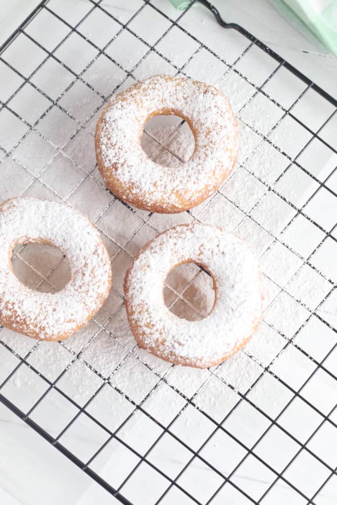 Powdered Sugar Biscuit Donuts on a wire baking rack.