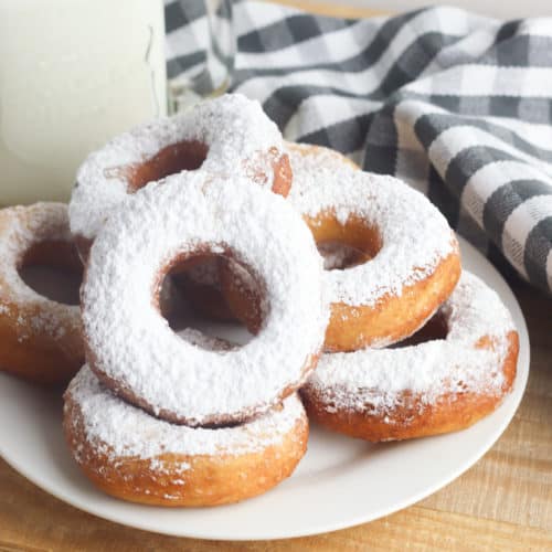 stack of powdered sugar biscuit donuts on a white plate