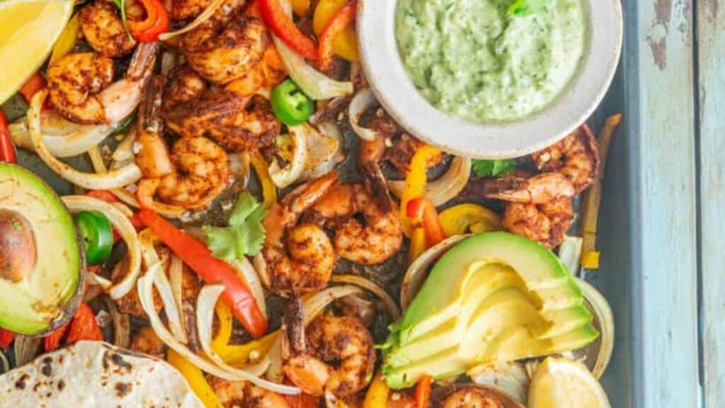 Sheet pan of shrimp fajitas with avocado slices, peppers and onions.