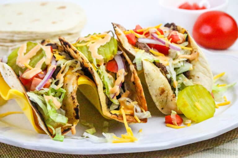 Three tacos on a plate with lettuce, tomatoes and cheese.