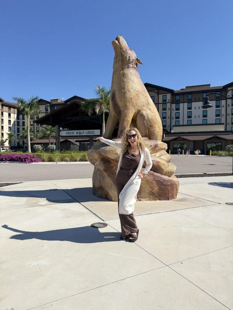 Large wolf sculpture at Great Wolf Lodge with woman posing in front, sunny day, modern resort background.